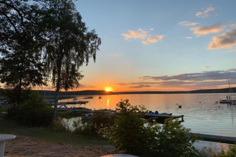 Atardecer sobre un lago tranquilo en Holiday home «Maryna», Alemania, con muelle, botes y árboles visibles.