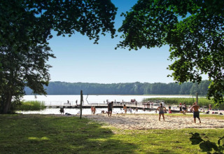 Feriehytte «Maryna» i Tyskland med udsigt over sø, strandvolleyball, badebroer og folk, sommerdag.