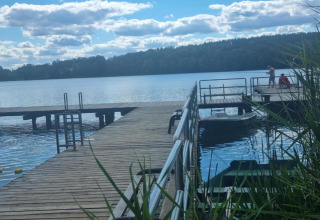 Vue sur un ponton en bois et un lac à Holiday home «Maryna» en Allemagne, avec des gens, des bateaux et une forêt.