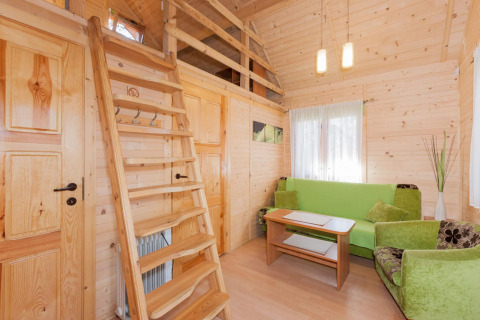 Interno di lodge in legno con divano verde, scala per il soppalco, tavolino e luce naturale tenue.