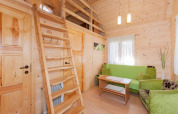 Cozy wooden lodge interior with green sofa, loft ladder, wooden table, and soft natural window light.