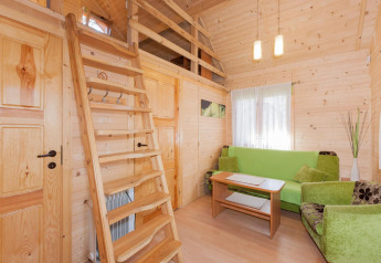 Gemütliches Ferienhaus mit Holzinterieur, grüner Couch, Holztreppe zur Galerie und heller Beleuchtung.