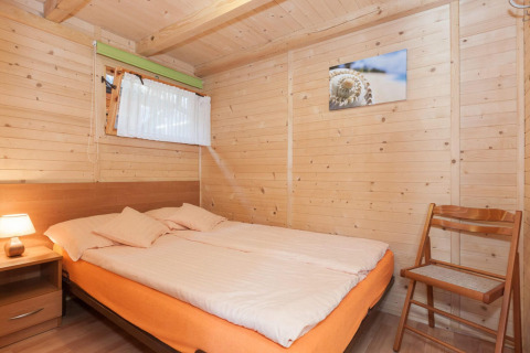 Camera da letto in legno con letto matrimoniale, sedia, comodino e quadro presso Domki letniskowe Pobierowo.