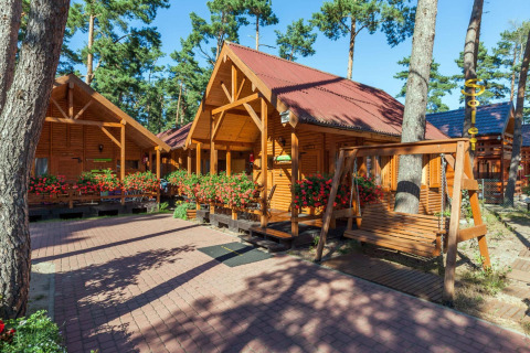 Baite di legno tra fiori e pini al lodge Domki letniskowe Pobierowo in Germania, con altalena in primo piano.