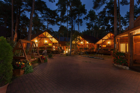 Bungalow in legno illuminati presso Domki letniskowe Pobierowo, circondati da alberi e fiori di sera in Germania.