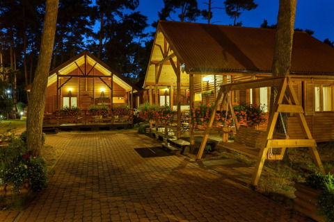 Vista serale di lodge in legno illuminati con fiori e altalena presso Domki letniskowe Pobierowo, Germania.