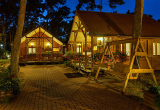 Vista serale di lodge in legno illuminati con fiori e altalena presso Domki letniskowe Pobierowo, Germania.