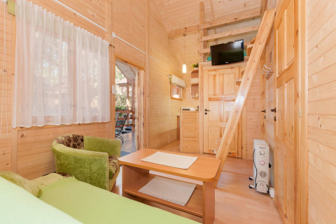 Accogliente interno di lodge in legno con poltrona verde, soppalco, scala e TV a Domki letniskowe Pobierowo.
