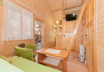 Acogedor interior de cabaña de madera con sillón verde, altillo, escalera y TV en Domki letniskowe Pobierowo.