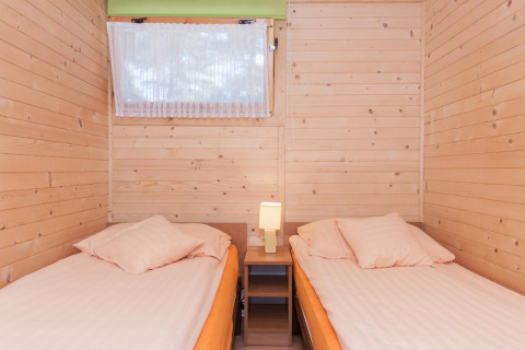 Due letti singoli con biancheria chiara in una stanza rivestita in legno presso il lodge Domki letniskowe Pobierowo.