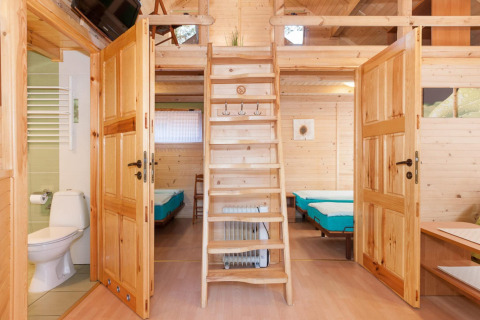 Interno di un lodge in legno con scala, porte aperte su camere da letto e bagno a Domki letniskowe Pobierowo.