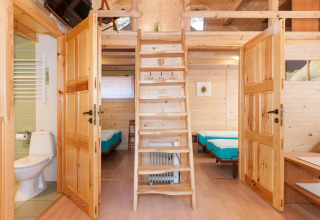 Interno di un lodge in legno con scala, porte aperte su camere da letto e bagno a Domki letniskowe Pobierowo.