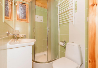 Bright bathroom with green tiles, shower cabin, toilet, small sink and towel warmer in Domki letniskowe Pobierowo.