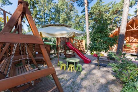 Parco giochi a Domki letniskowe Pobierowo con scivolo rosso, altalene, tavolini e panchine in legno.