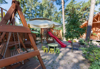 Parco giochi a Domki letniskowe Pobierowo con scivolo rosso, altalene, tavolini e panchine in legno.