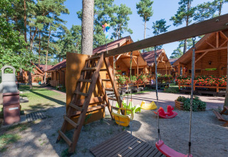 Parco giochi con altalene e casette di legno a Domki letniskowe Pobierowo, tra pini e fiori colorati.