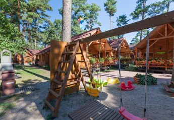 Aire de jeux avec balançoires et chalets en bois à Domki letniskowe Pobierowo, entouré de pins et de fleurs.