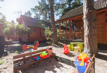 Spielplatz mit Sandkasten, Spielzeug und Holzhütten bei Sonnenlicht im Domki letniskowe Pobierowo Lodge in Deutschland.