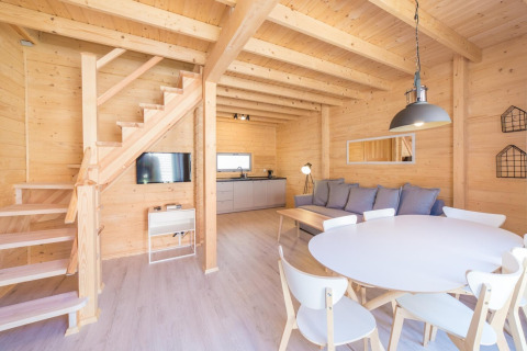 Bright wooden holiday cottage with modern kitchen, dining table, sofa, and staircase in Pobierowo, Germany.