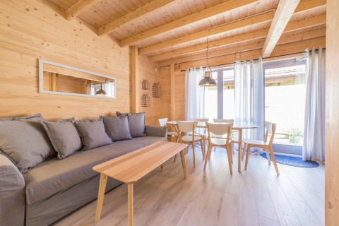 Licht houten vakantiewoning in Pobierowo, Duitsland, met grijze zetel, eettafel en veel ramen.