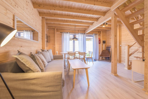 Modern wooden holiday cottage in Pobierowo, Germany with bright interior, sofa, dining area, and stairs.