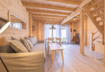 Modern wooden holiday cottage in Pobierowo, Germany with bright interior, sofa, dining area, and stairs.