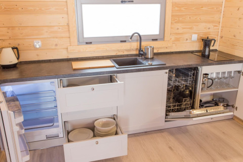 Moderne Küche mit Holzverkleidung, offenen Schubladen, Geschirrspüler, Kühlschrank und Geschirr.