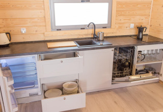 Moderne keuken met houten wanden, open lades, vaatwasser en koelkast in vakantiehuisje zichtbaar.