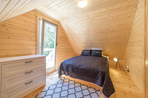 Gemütliches Schlafzimmer im Holzferienhaus mit großem Bett, Kommode und Fensterblick ins Grüne.