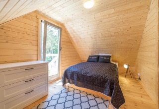 Slaapkamer in houten lodge met tweepersoonsbed, grote kast en ruim raam met uitzicht op het groen.