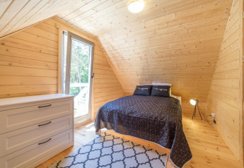 Chambre chaleureuse en bois dans un chalet avec lit double, commode et grande fenêtre sur la nature.