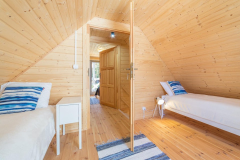 Gezellige houten kamer met twee enkele bedden, blauwe kussens en een openstaande deur in het midden.