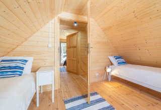 Cozy wooden bedroom in a cottage with two single beds, blue-striped pillows, and a central open door.