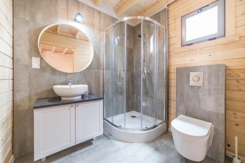 Modern bathroom of a wooden holiday lodge, featuring a round mirror, shower cabin, sink, and toilet.