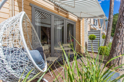 Buitenterras aan vakantiehuisje in Pobierowo met hangstoel, tuintafel en gestreepte zonnekap.