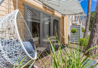 Buitenterras aan vakantiehuisje in Pobierowo met hangstoel, tuintafel en gestreepte zonnekap.