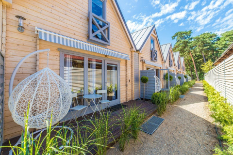 Wooden holiday cottages with patios, garden chairs, and hanging swings at Pobierowo lodge in Germany.