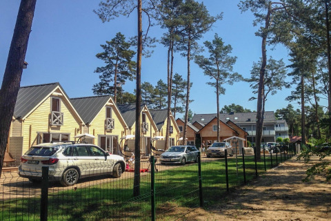 Holiday cottages for 5 people in Pobierowo, surrounded by pine trees, parked cars, and clear blue sky.
