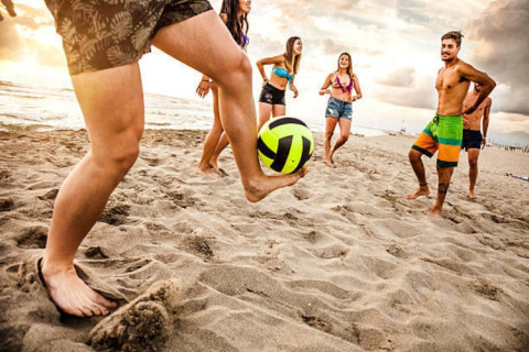 Groep jonge mensen speelt bal op het zandstrand bij zonsondergang aan een glampingverblijf.