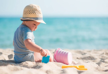 Jong kind met hoedje speelt met strandspeelgoed op het zand aan zee bij een glamping-accommodatie.