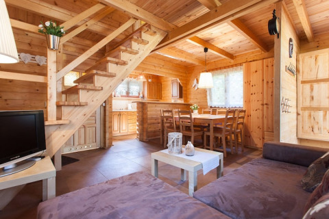 Acogedora sala de estar con interior de madera, sofá, mesa de comedor y escalera en Wooden holiday cottages Pobierowo, Alemania.