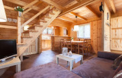 Acogedora sala de estar con interior de madera, sofá, mesa de comedor y escalera en Wooden holiday cottages Pobierowo, Alemania.