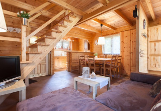 Knusse woonkamer met houten interieur, sofa, eettafel en trap bij Wooden holiday cottages Pobierowo, Duitsland.