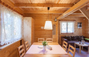 Helles, holzgetäfeltes Interieur eines gemütlichen Ferienhauses mit Esstisch, Sofa und Spitzengardinen.