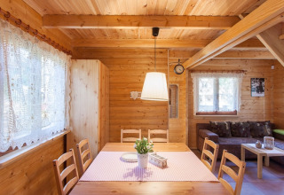 Helles, holzgetäfeltes Interieur eines gemütlichen Ferienhauses mit Esstisch, Sofa und Spitzengardinen.