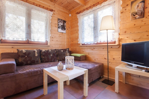 Gezellige houten woonkamer met bruine zetel, kanten gordijnen en tv in Wooden holiday cottages Pobierowo.