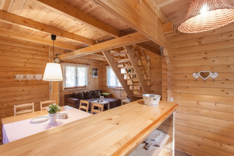 Interieur van een houten vakantiehuisje met gezellige zithoek, eettafel en trap naar de bovenverdieping.