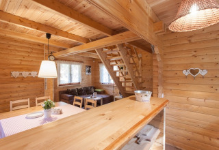 Interieur van een houten vakantiewoning met knusse zitruimte, eettafel en trap naar de mezzanine.