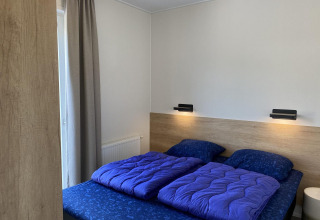 Moderne slaapkamer in Zonneweelde Lodge Deluxe op Camping Zonneweelde in Nederland, met blauw bedlinnen.