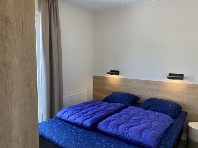 Dormitorio moderno en Zonneweelde Lodge Deluxe de Camping Zonneweelde, Países Bajos, con ropa de cama azul.